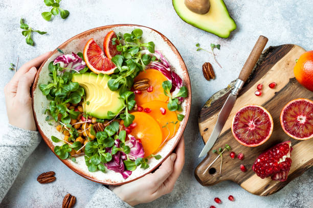 A vegetable salad with avocado, pomegranate, and nuts, a chopping board, and knife on the side