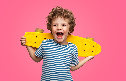 A laughing kid holding a yellow skater on his back with pink background